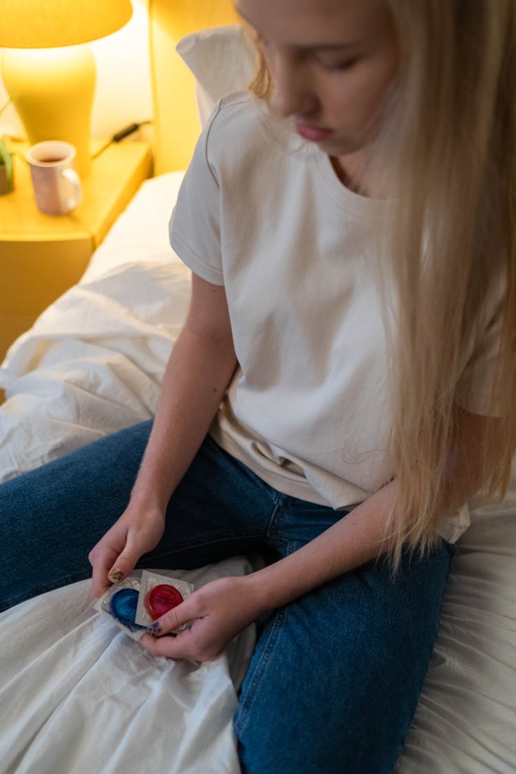 Woman In White Shirt Sitting On Bed Holding Condoms 