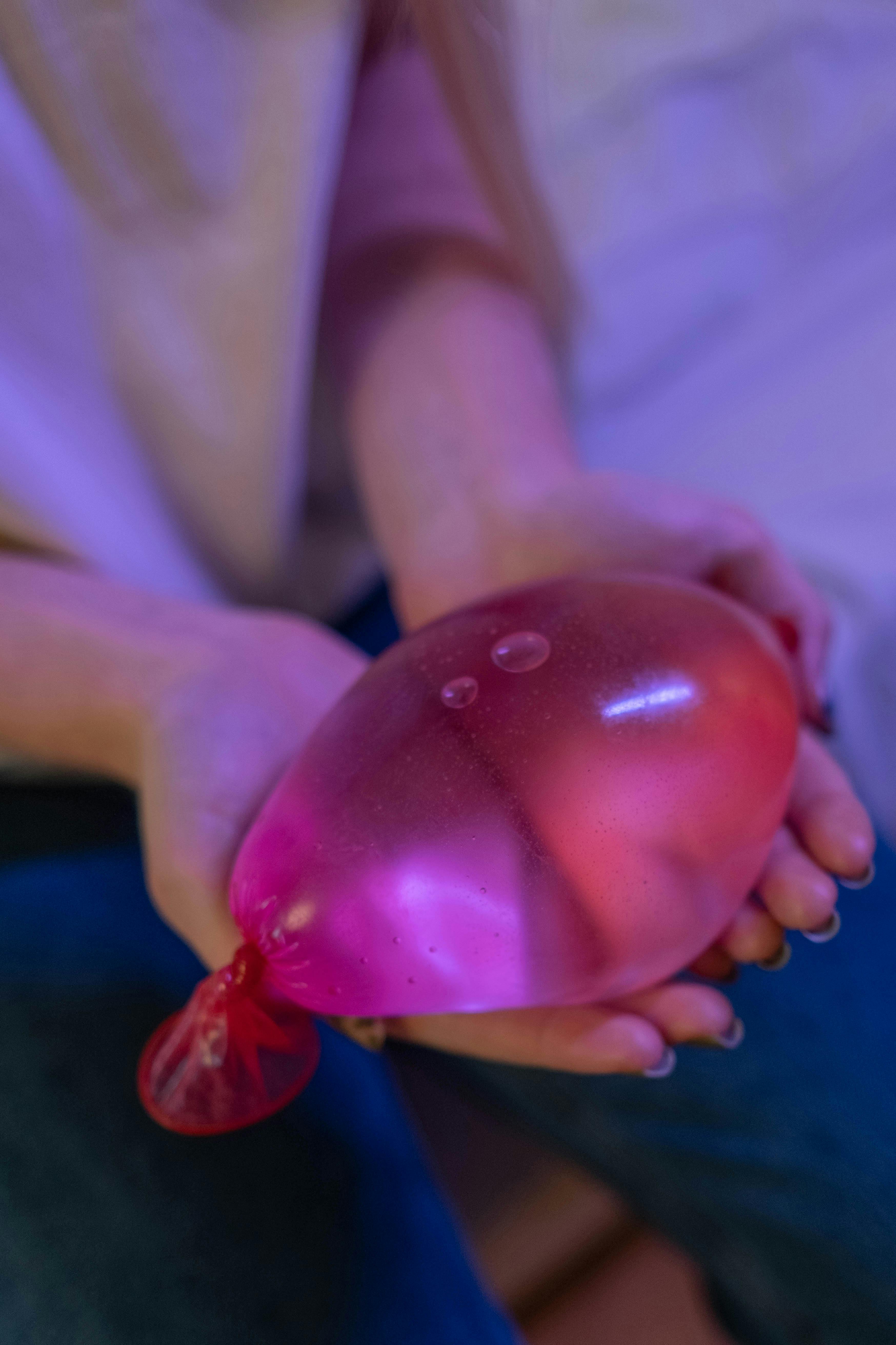 person holding pink condom with water