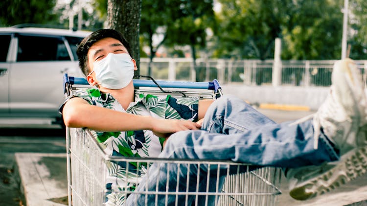 Young Asian Man Lying In Shopping Cart On Street