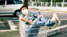 Young Asian man lying in shopping trolley on parking
