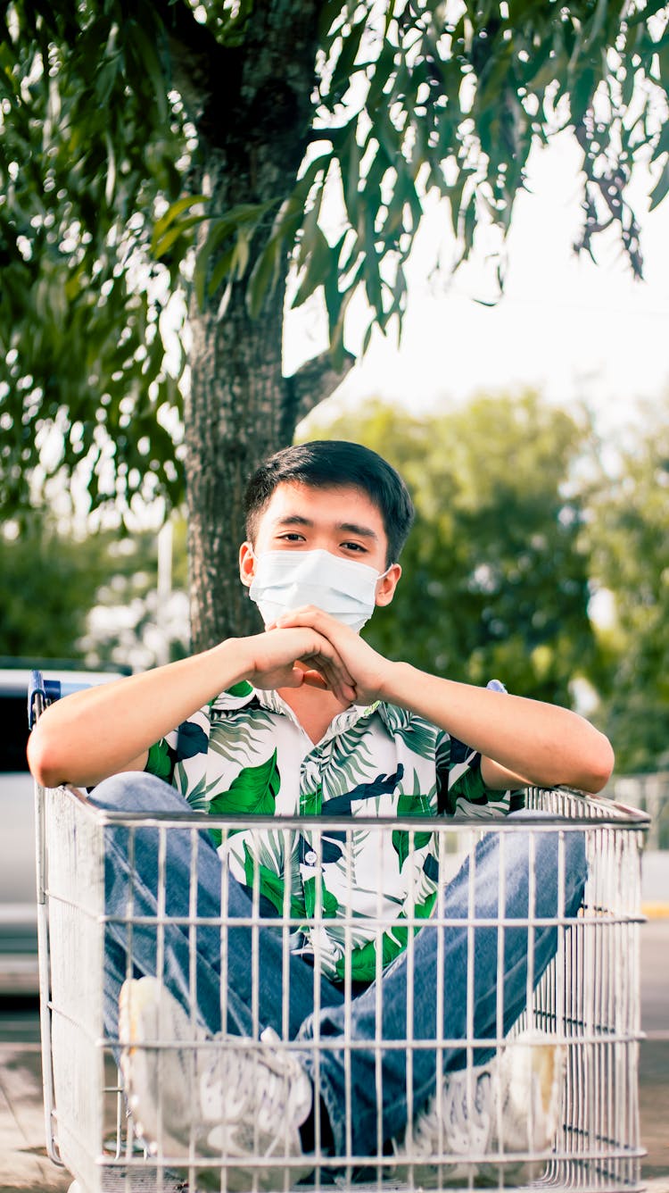 Positive Asian Man Sitting In Shopping Cart On Street