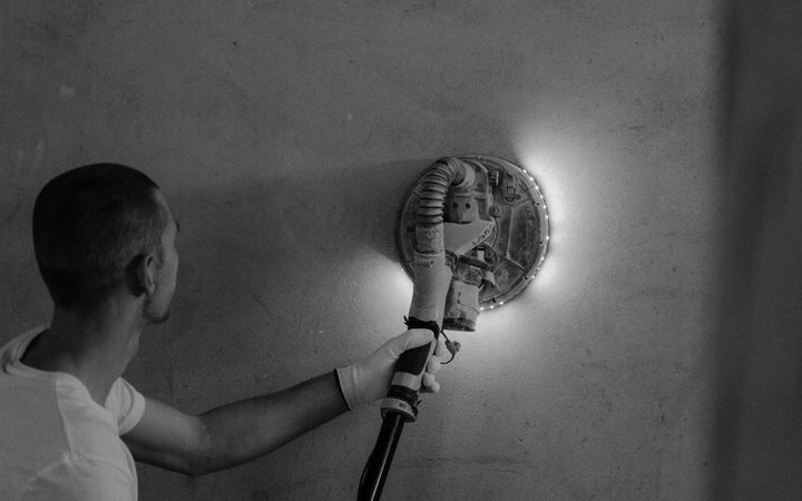 A handyman uses a polishing tool on an interior wall to renovate a home.