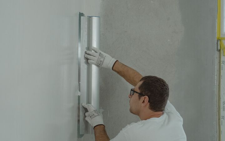 A man skillfully renovates a wall using tools in a modern interior setting.