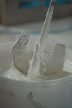 Detailed view of a paint mixer stirring white paint in a bucket, capturing texture and movement.