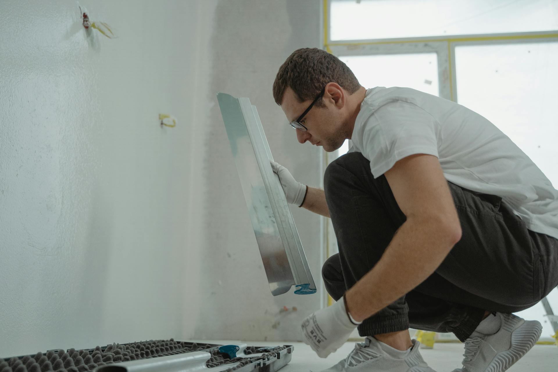 Adult male using metal trowel in interior home renovation project. White walls.