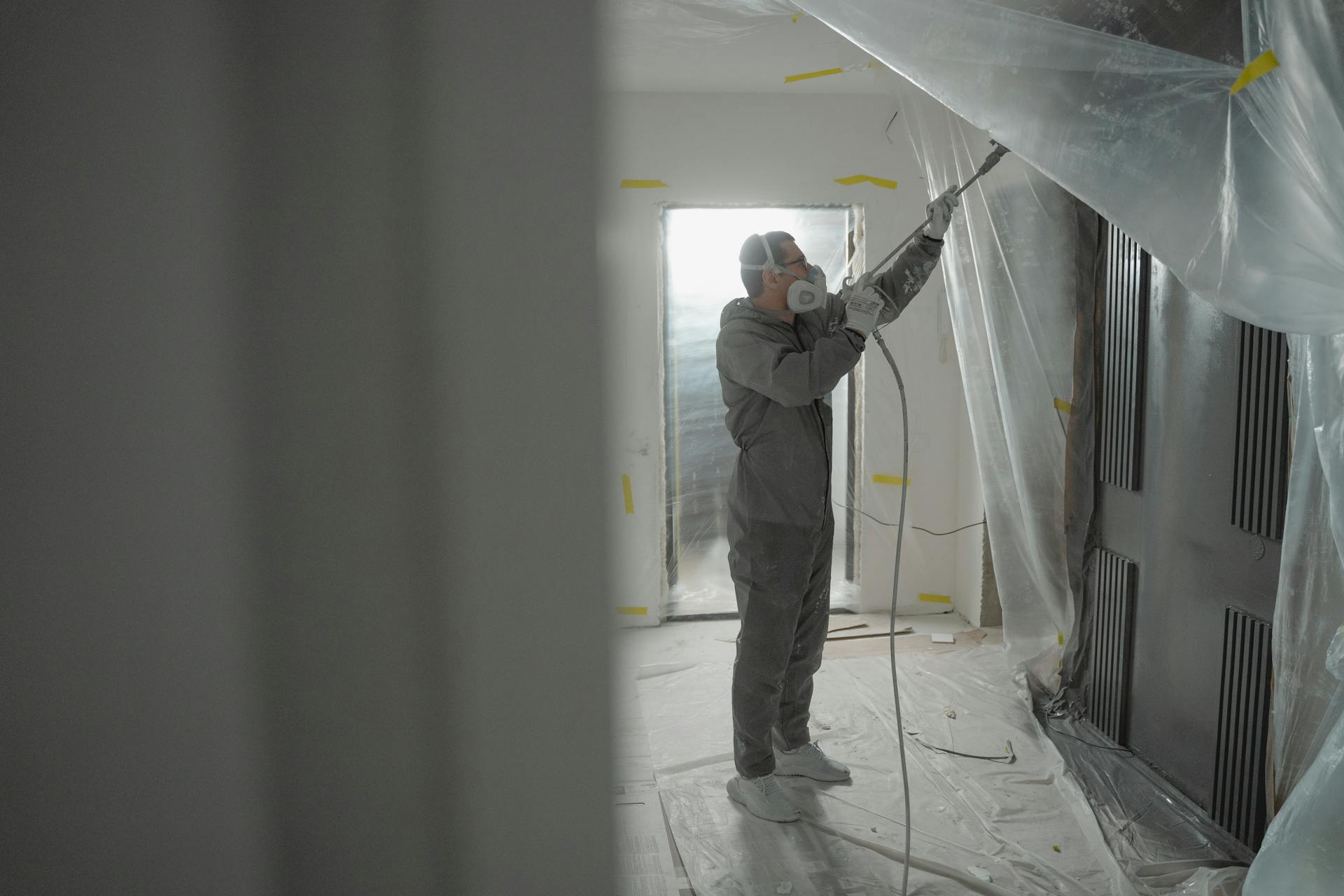 Man in protective gear spray painting a house's interior during renovation work.