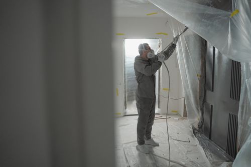 Free Man in protective gear spray painting a house's interior during renovation work. Stock Photo