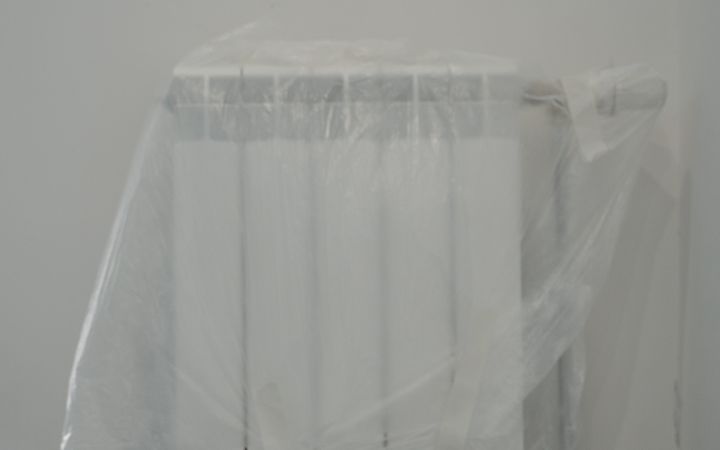 A radiator protected by plastic wrap, indoors, prepared for renovation.