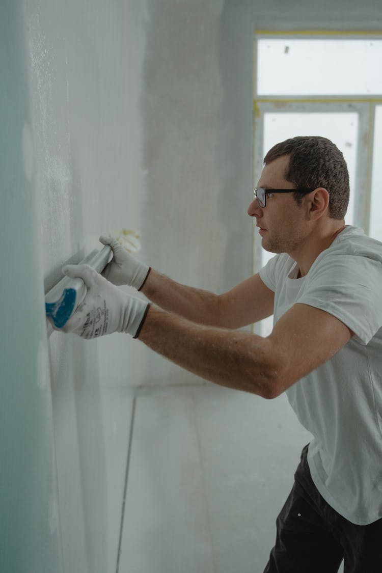 A Man In White Shirt Painting A House