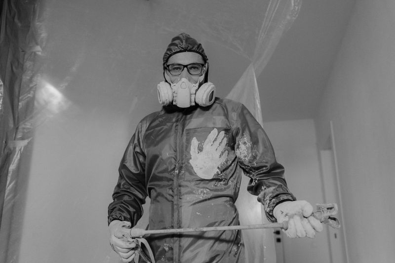 Painter in a full protective suit, respirator, and goggles holding a spray hose