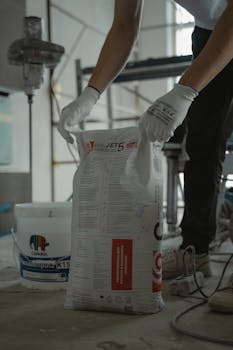 Worker handling cement bag in an indoor renovation project, wearing gloves for safety.