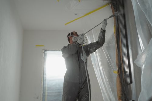 Free A professional painter wearing protective gear spray paints a wall indoors, working on a home renovation project. Stock Photo