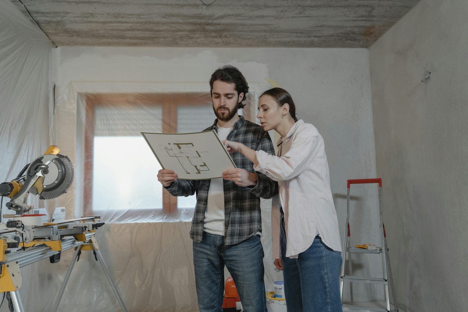 Man and woman reviewing floor plans in a home renovation setting, discussing project details.