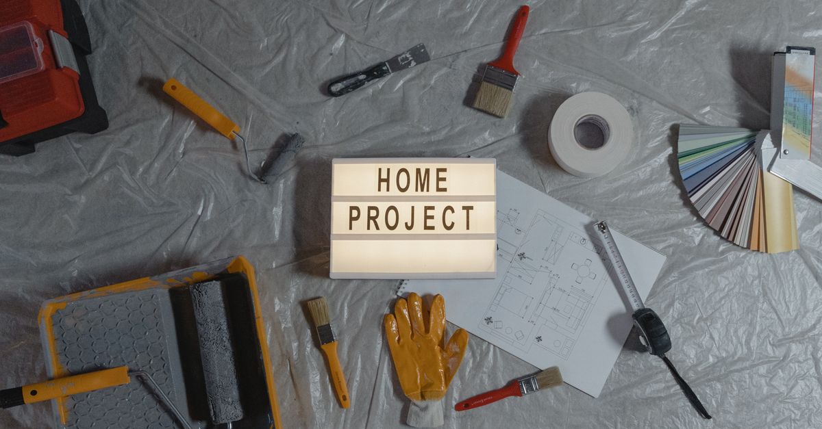 Flat lay of home improvement tools, paint samples, and blueprints for a DIY project.