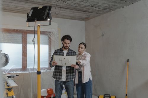 Free A couple examines blueprints in a partially renovated room, planning home improvements. Stock Photo