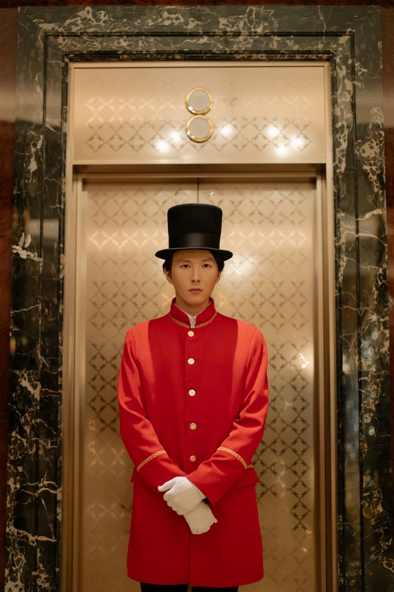 A doorman in classic attire standing in front of a luxurious hotel elevator.