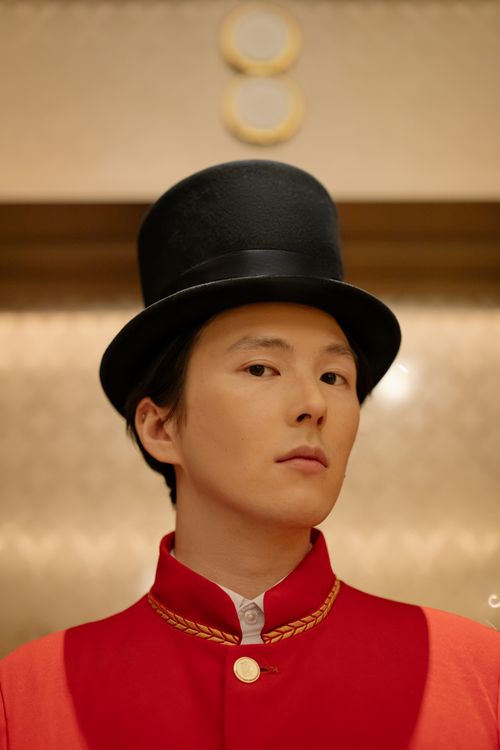 Free Elegant portrait of a doorman in a red uniform and top hat indoors. Ideal for hotel service themes. Stock Photo