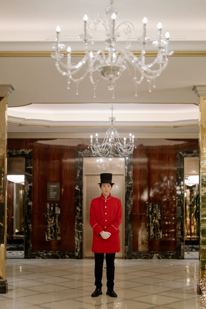 A uniformed concierge in a luxurious hotel lobby with chandeliers and marble decor.