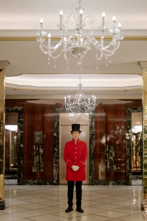 Free A uniformed concierge in a luxurious hotel lobby with chandeliers and marble decor. Stock Photo