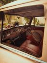 Through opened window of old timer automobile with leather seats and steering wheel with toys on shabby dashboard parked on street
