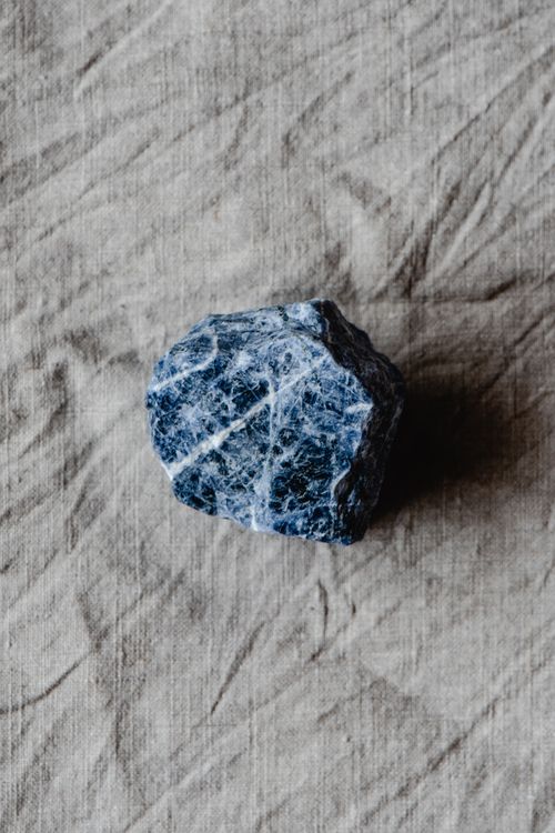 Free A solitary blue gemstone placed on a textured fabric creates an artistic contrast. Stock Photo