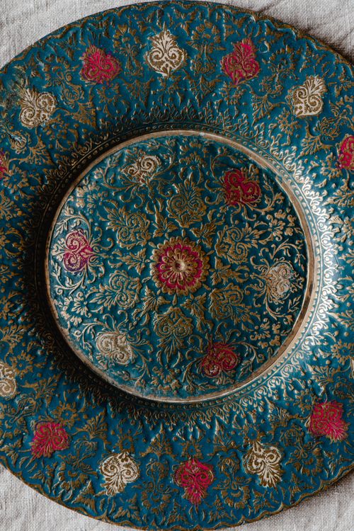 Free Close-up of a detailed ornate decorative plate with gold and red floral patterns on a teal background. Stock Photo