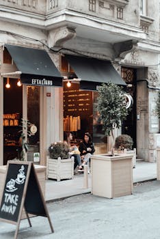Female friends in trendy clothes sitting and talking near cafe entrance and old building in city street on pavement near road in daytime