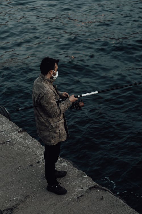 Unrecognizable fisherman with rod fishing in rippled river