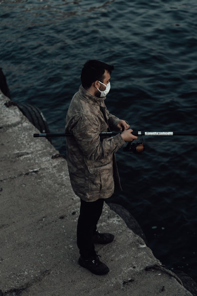 Unrecognizable Fisherman In Mask Catching Fish In Lake