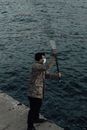 Anonymous fisherman in sterile mask casting rod against river