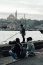 Anonymous ethnic couple speaking against man catching fish with rod in Bosporus River in Istanbul Turkey