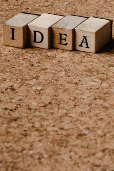 Wooden letter blocks spelling 'IDEA' on a cork background, symbolizing creativity.