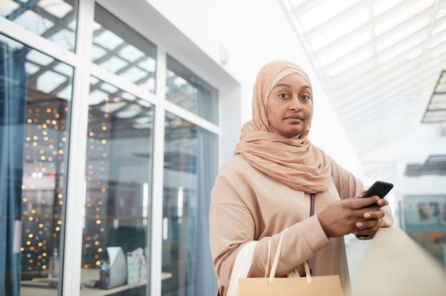 Woman in a headscarf holding a phone and a shopping bag
