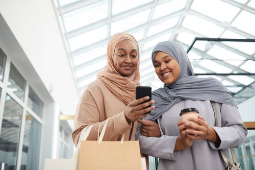 Free Two women in hijabs sharing a moment while shopping indoors, smiling and looking at a phone. Stock Photo