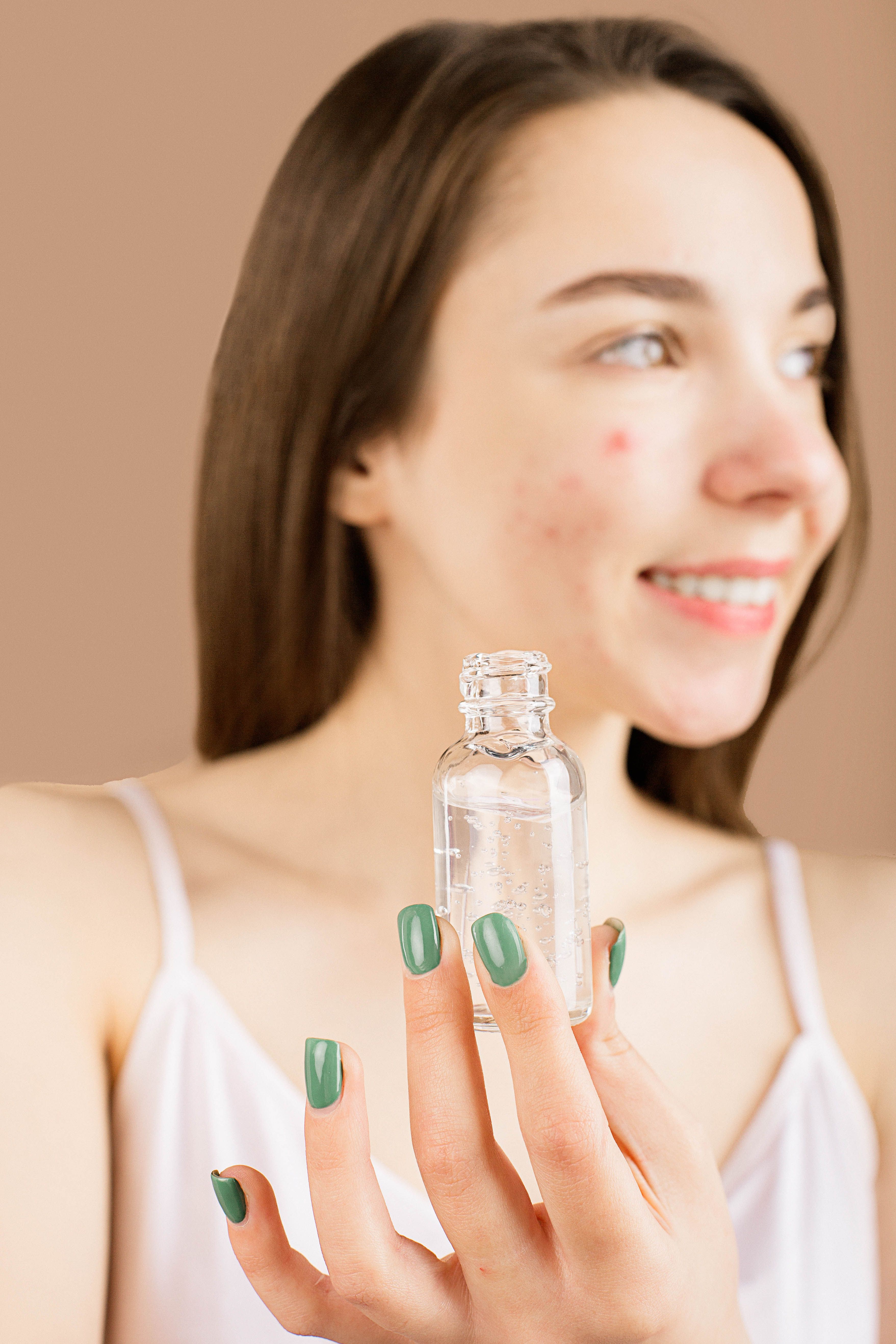 Smiling young woman with clear skin holds a small glass cosmetic bottle, symbolizing natural beauty.