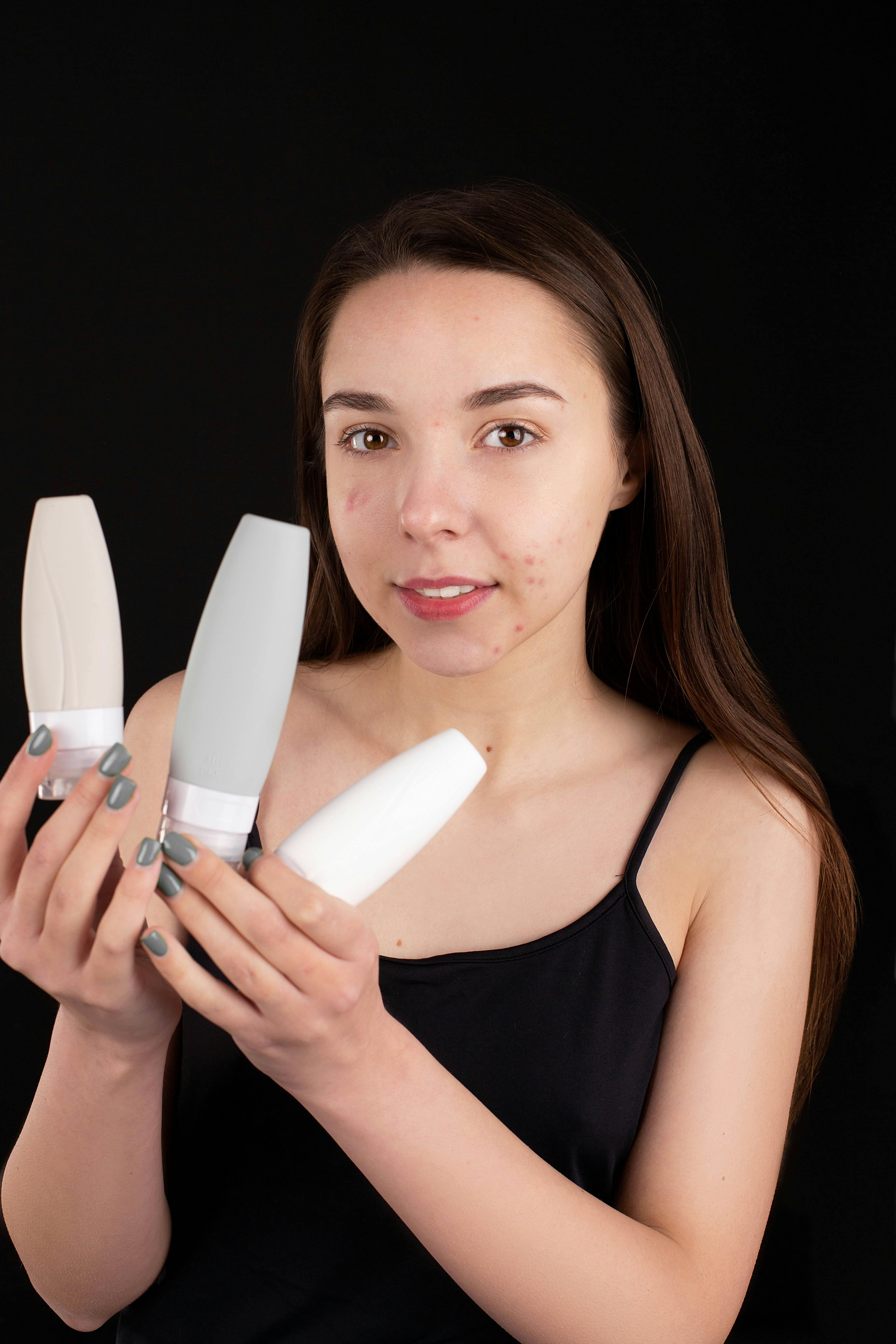 Young girl holding skincare bottles, focusing on her skincare routine against a black background.