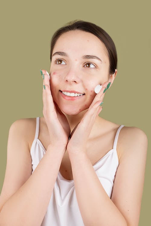 Free Smiling Teenager Applying a Facial Cream on Her Face Stock Photo