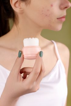 Close-up of a woman using a facial brush to care for acne-prone skin.