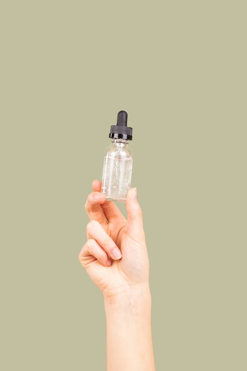 Person Holding Clear Glass Bottle with Dropper