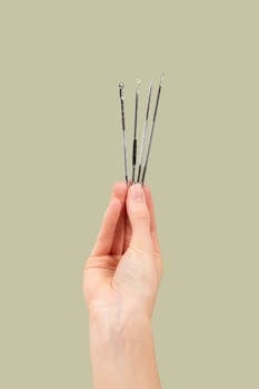 Close-up of a hand holding metal dermatological tools against a light green background.