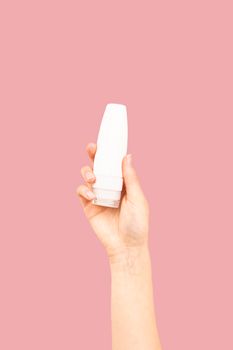 A close-up of a hand holding a white cosmetic bottle against a pink background, ideal for beauty and skincare themes.