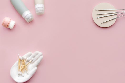 Collection of skincare tools and products arranged on a pastel pink surface in a flat lay style.