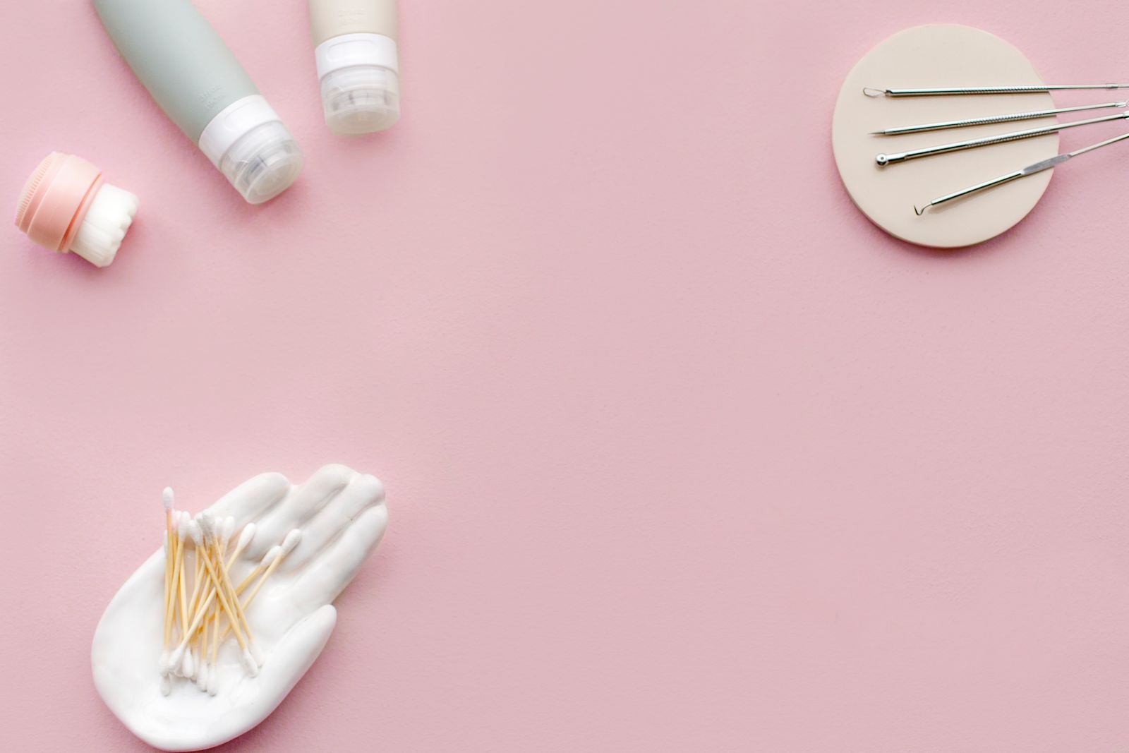 Curated skincare tools and cosmetic products on a warm pink surface