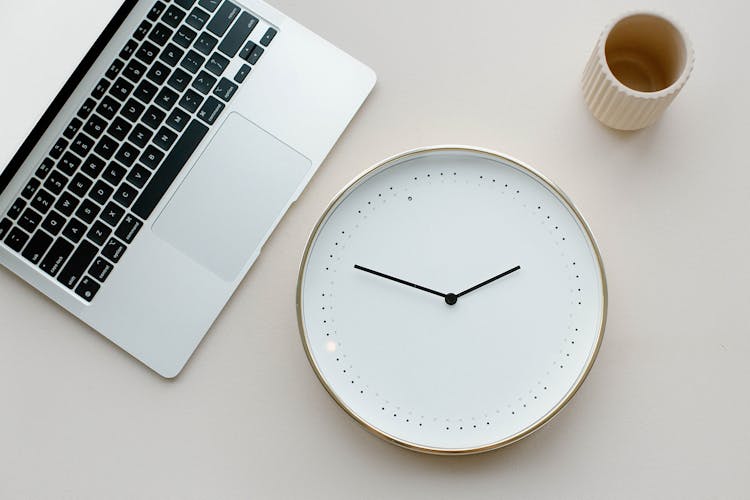 Close-Up Shot Of An Analog Clock Beside A Laptop