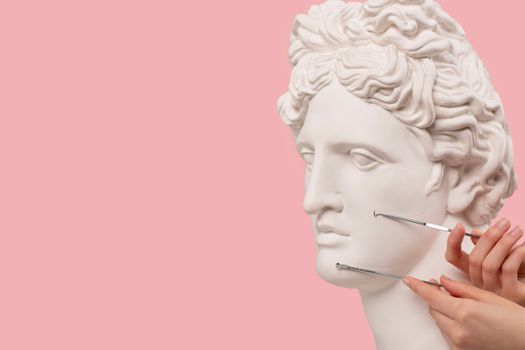 Classical bust with beauty tools on pink background, merging art with skincare.