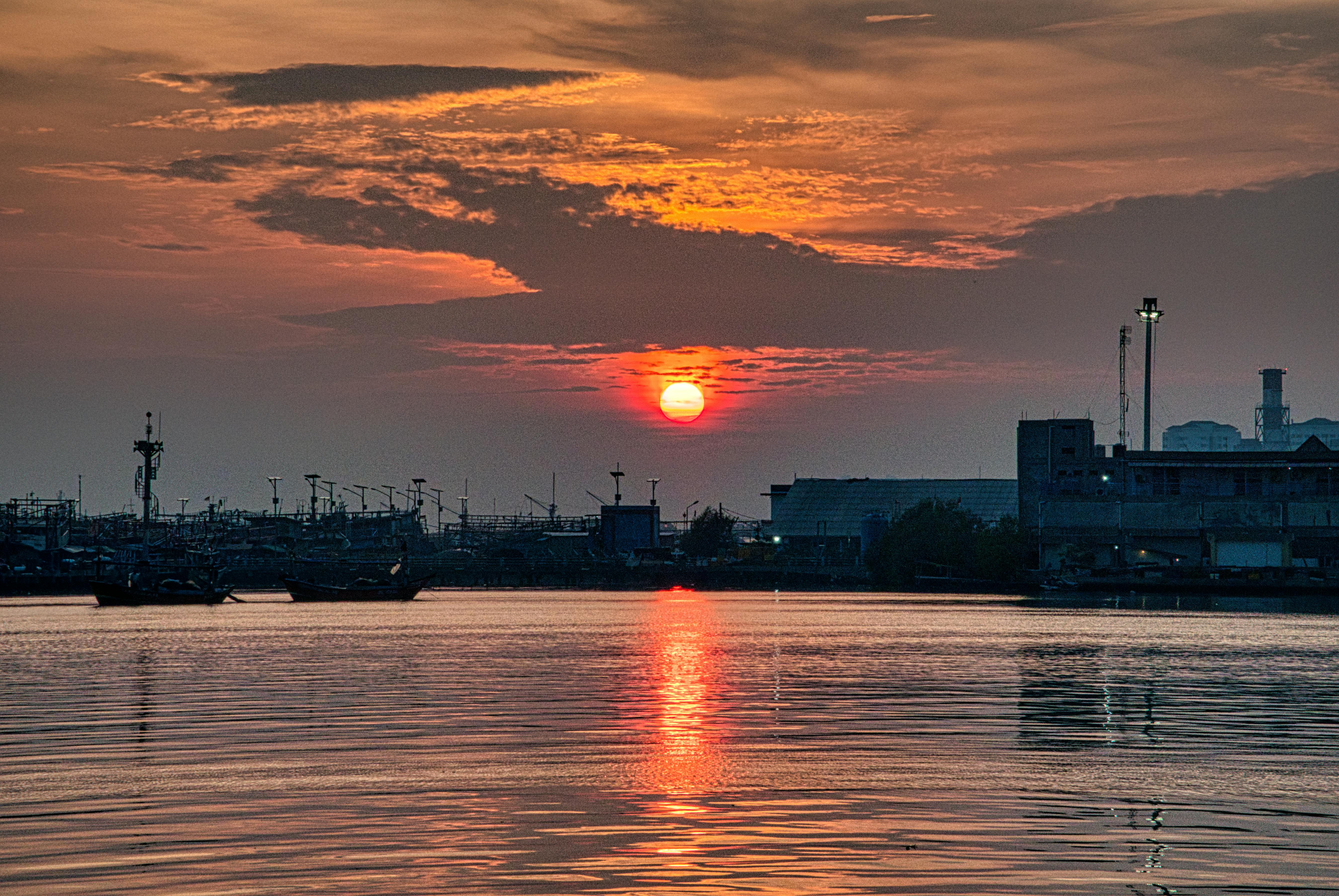 Dramatic sunset over Jakarta harbor with vivid sky reflection on calm sea.