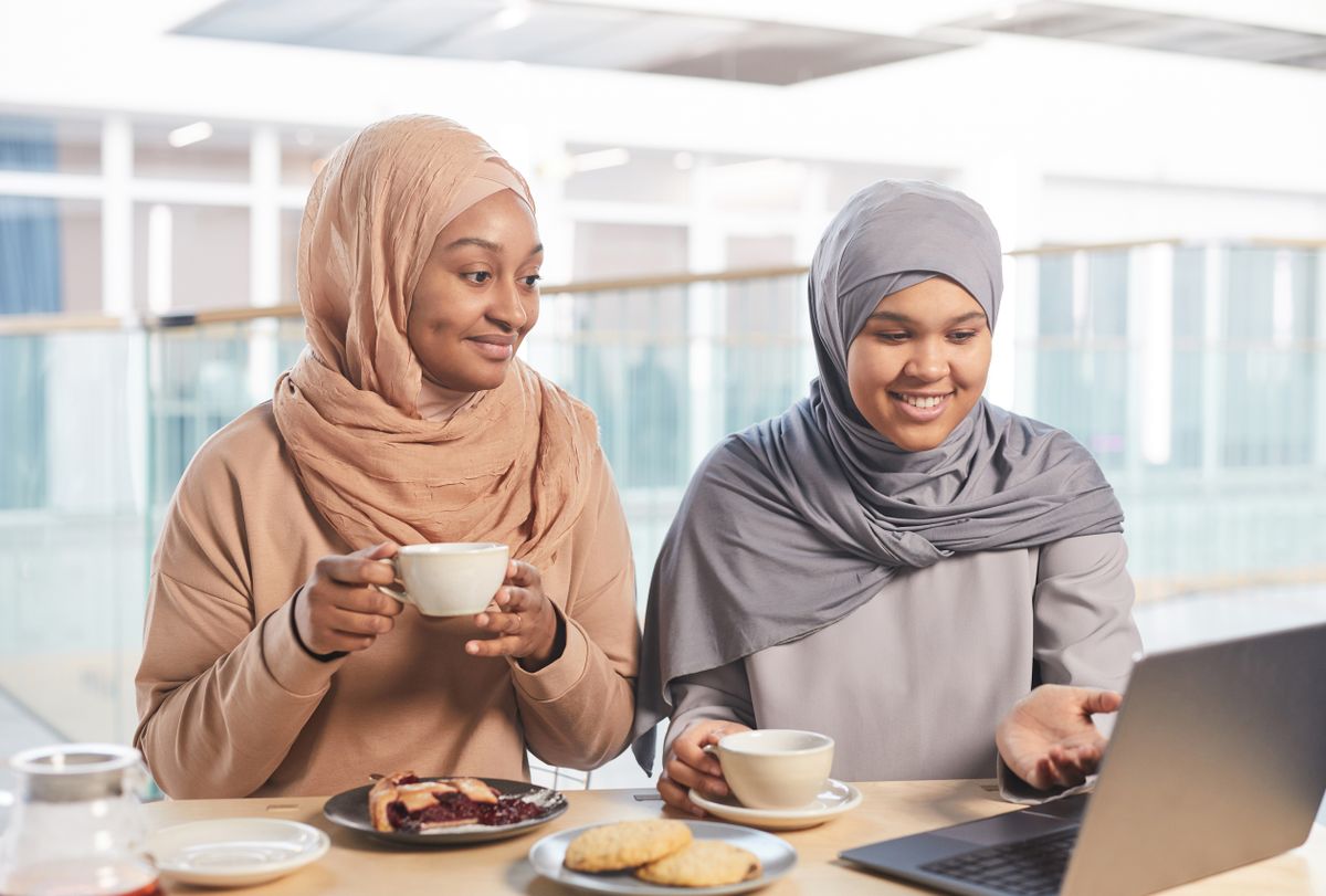 امرأتان ترتديان الحجاب تتناولان القهوة بجانب حاسوب
