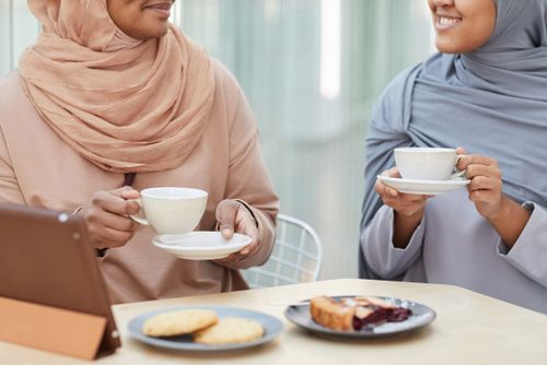 Free Two women in hijabs enjoy coffee and pastries, showing friendship and cultural attire. Stock Photo