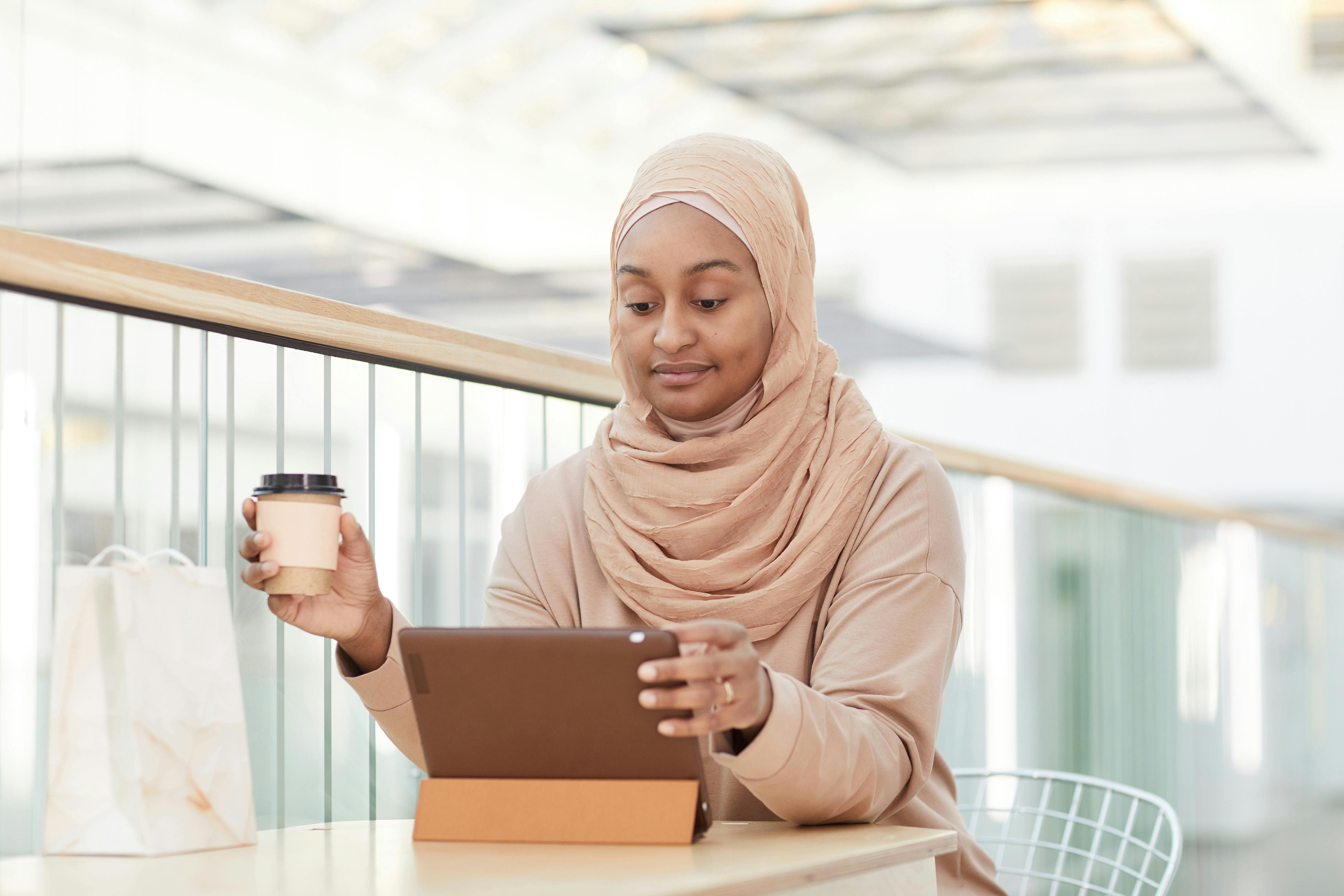 woman in beige hijab holding a coffee cup