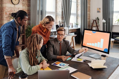 Free A Group of People Discussing Beside a Desktop with Graph on Screen Stock Photo